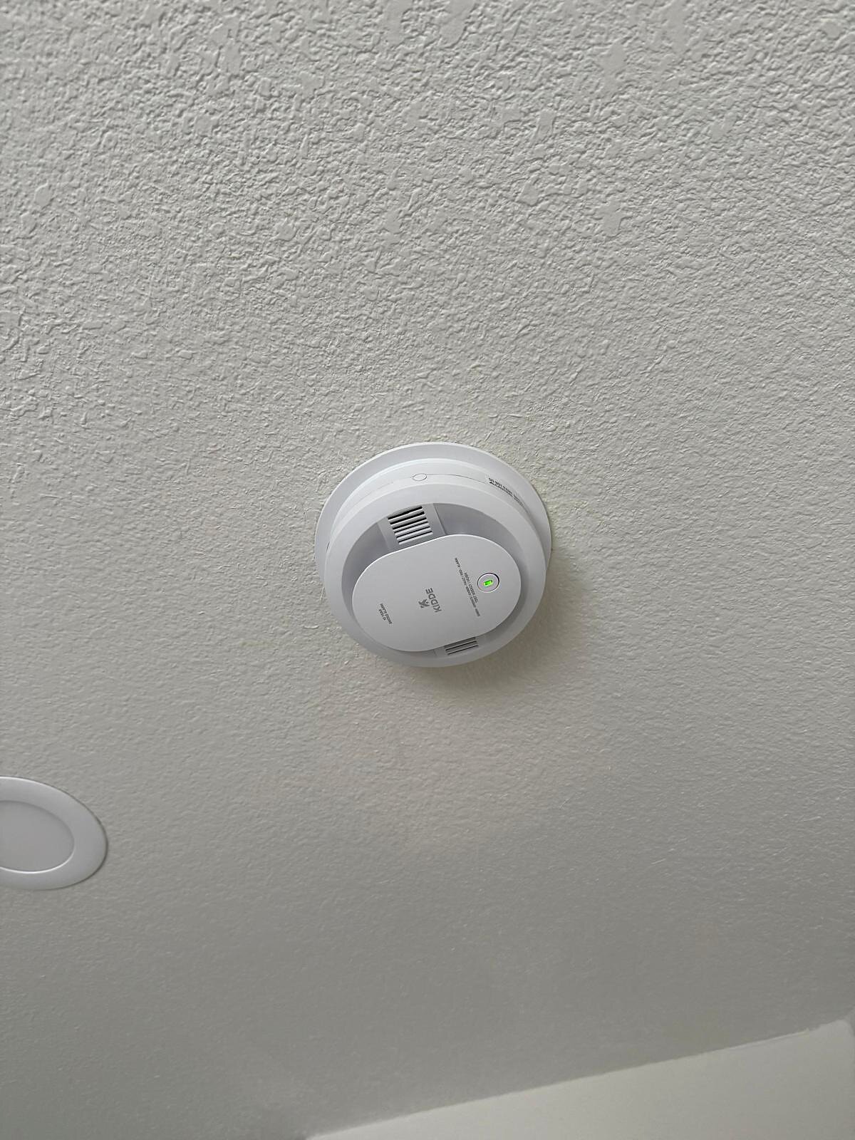 Close-up of a new Kidde smoke detector installed on the ceiling, green status light lit