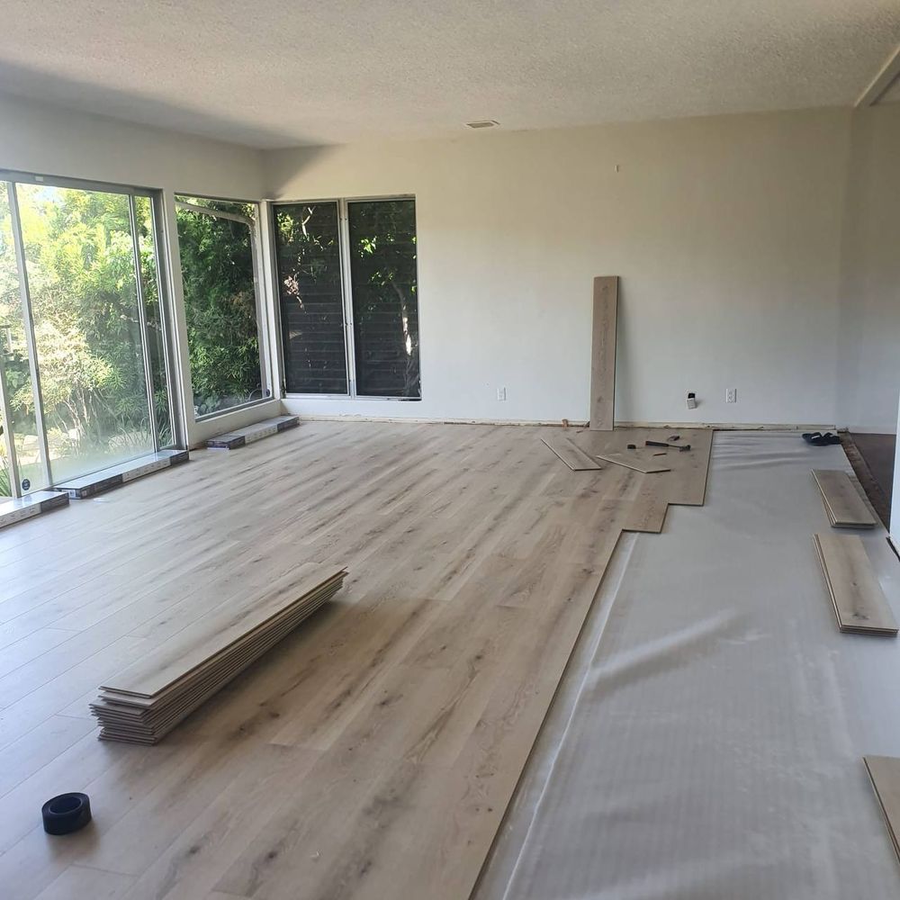 Wide-plank laminate flooring going down over underlayment in a bright living room mid-installation