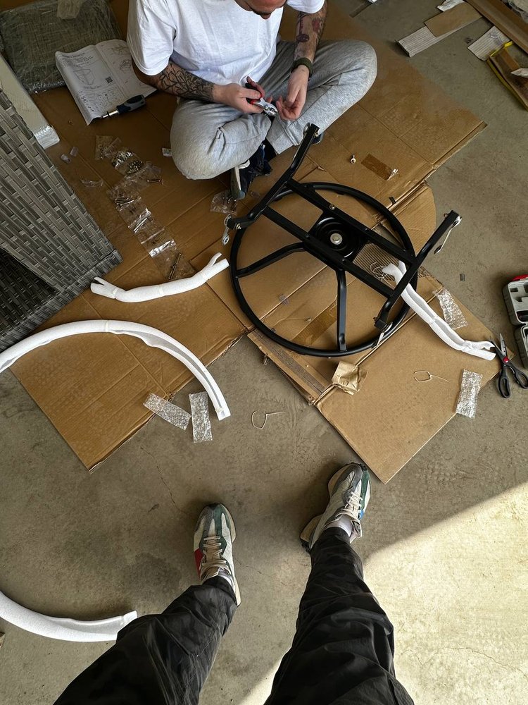 Denver Handy Co. technician sorting hardware and frame parts on cardboard while assembling a patio chair in a garage