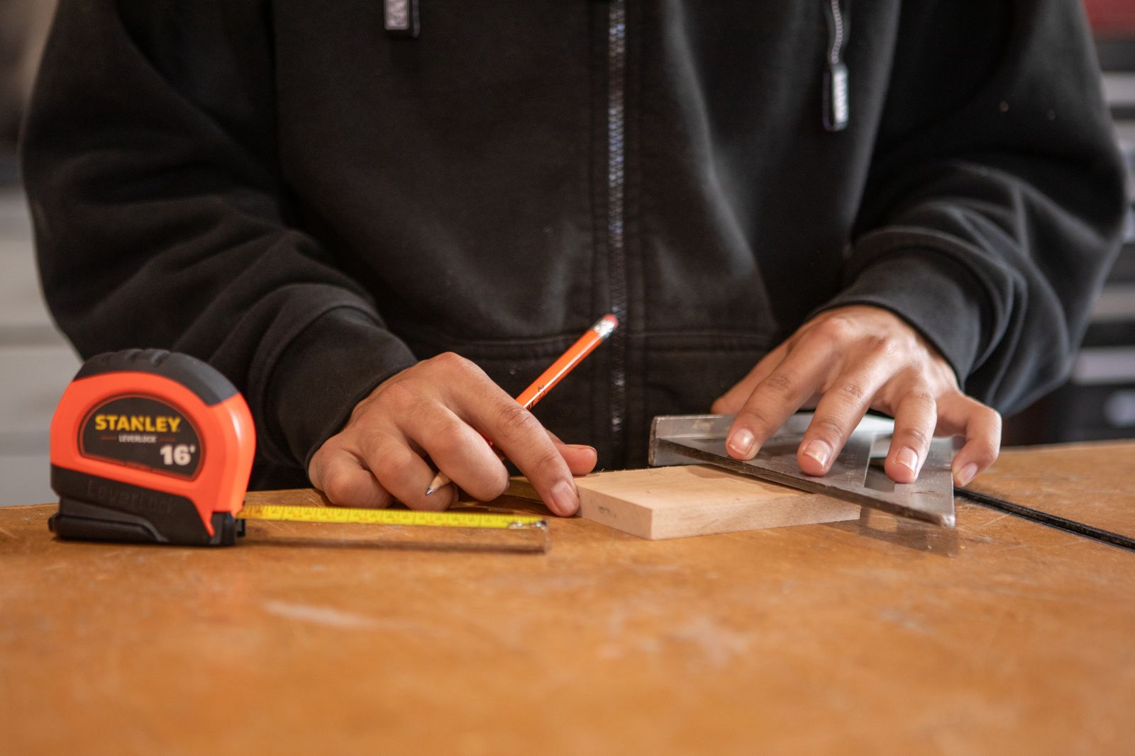 Carpenter measuring a wood block with a tape measure and speed square