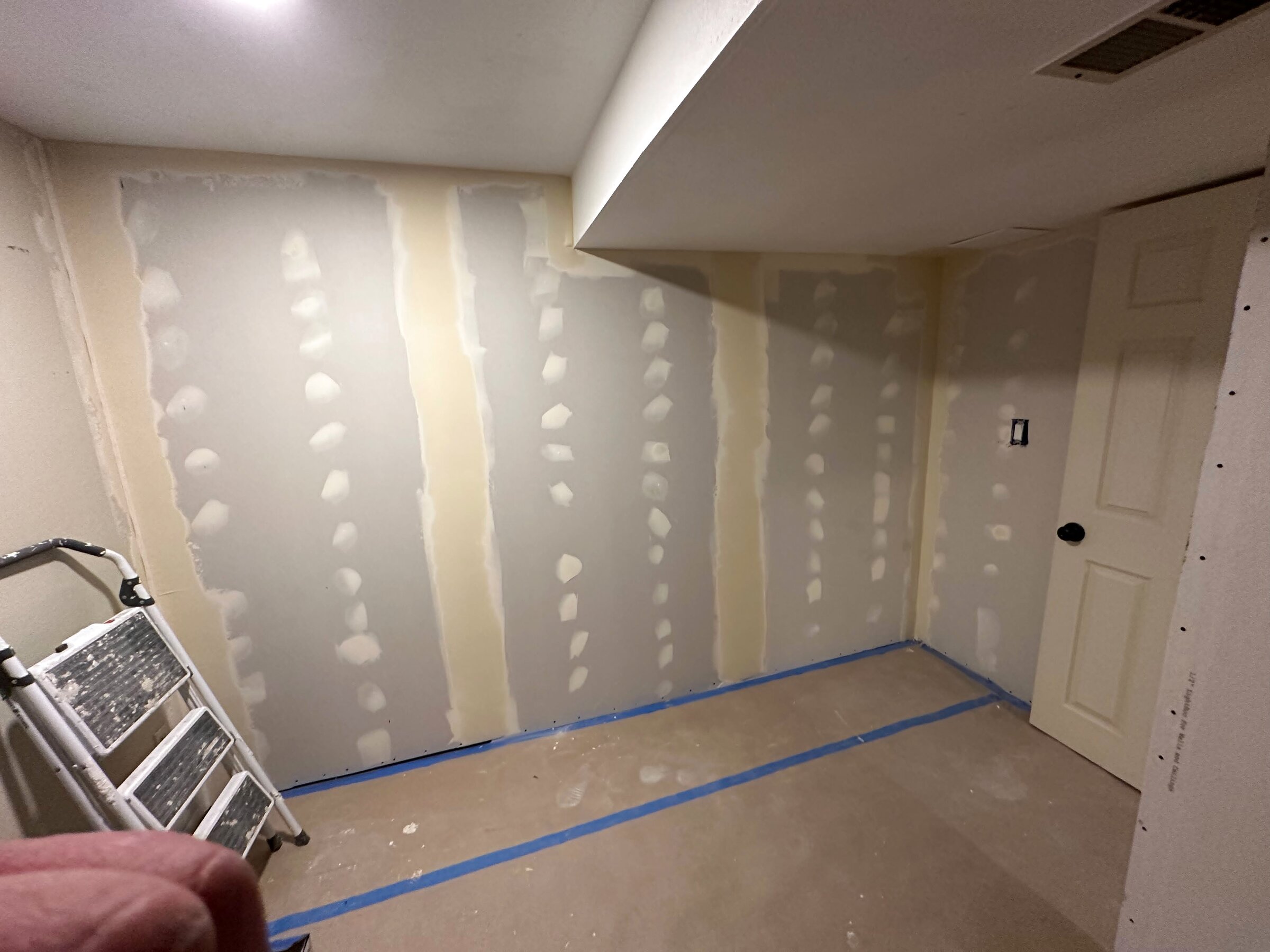 Basement's freshly taped and mudded drywall seams, ladder set up for the next coat