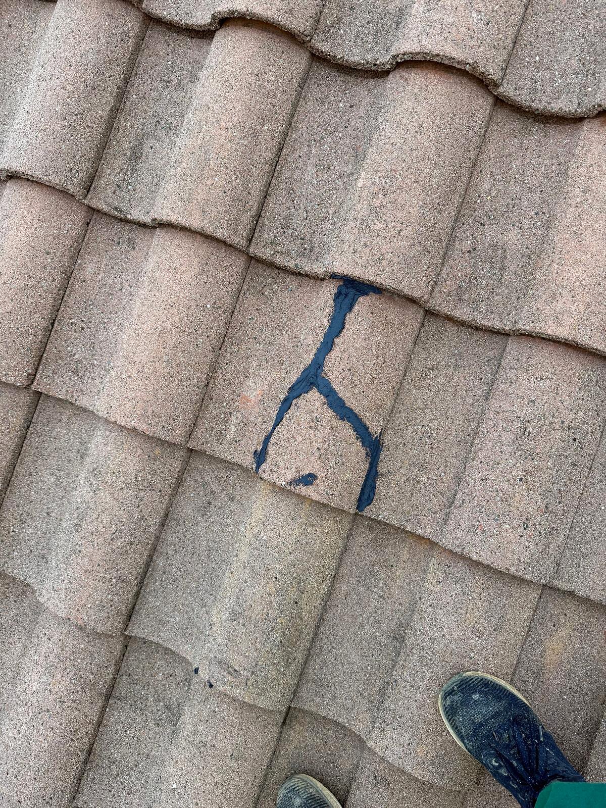 Cracked concrete roof tile sealed with dark roofing sealant to stop water intrusion