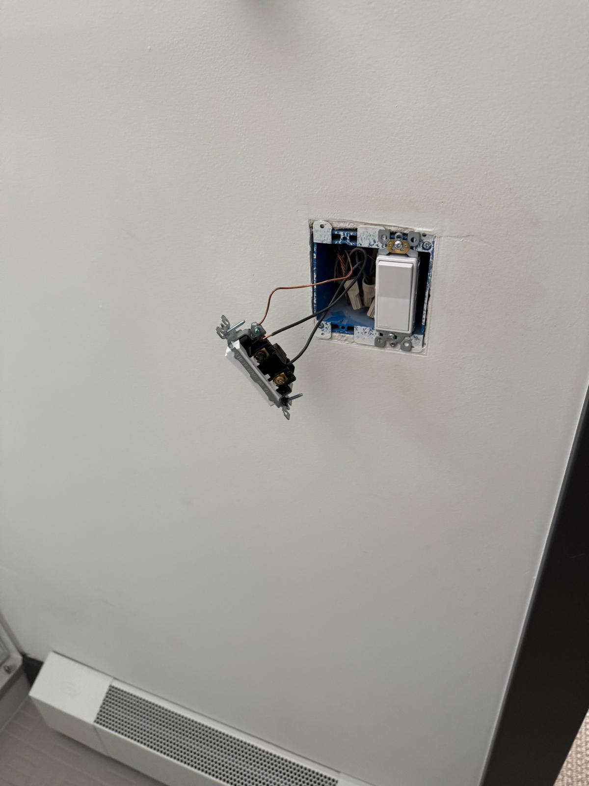 Wall switch pulled from the box mid-swap, showing the wiring behind a two-gang electrical box