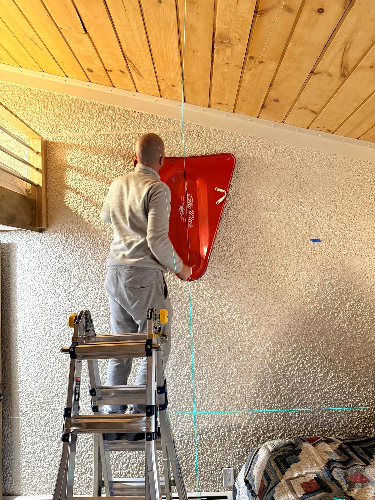 Closer view of the red sled being leveled and secured to the accent wall with laser guide lines still visible