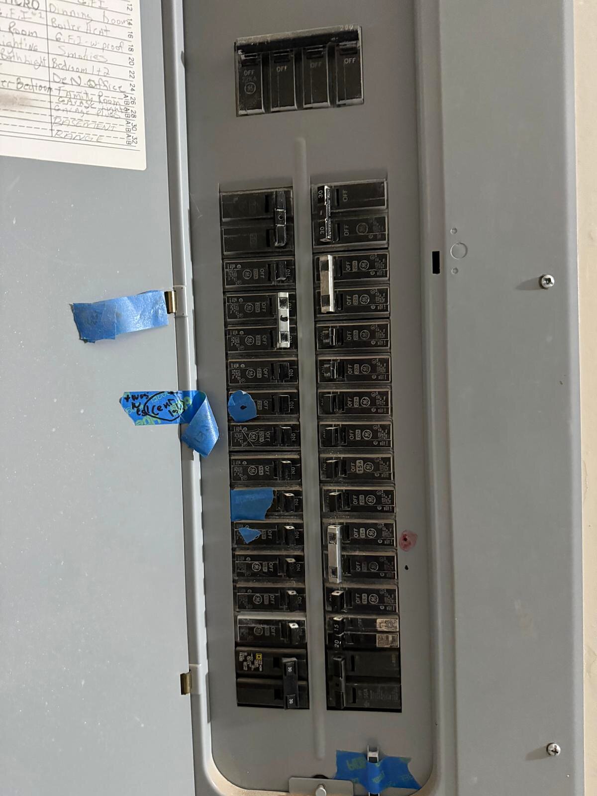 Open electrical panel with breakers labeled by room, blue tape marking circuits worked on during the visit