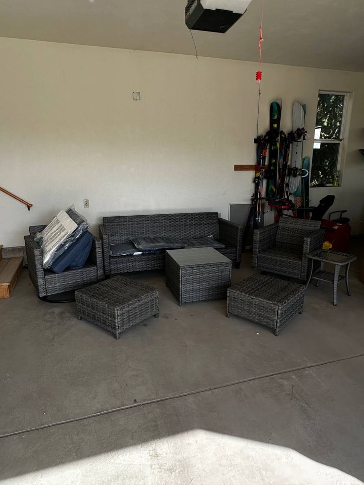 Fully assembled gray wicker patio set with sofa, chairs, ottomans and table in a garage