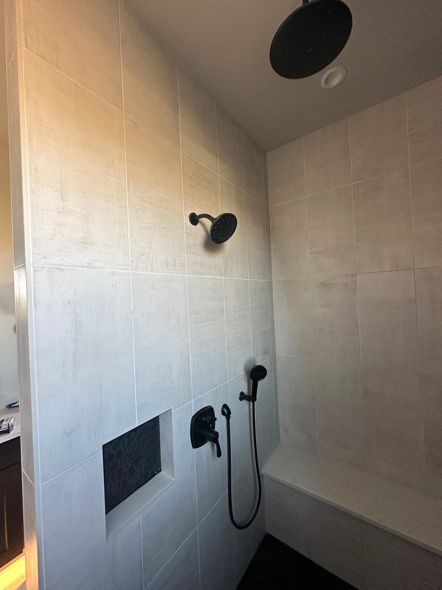 Finished walk-in shower with matte black rain-head and handheld fixtures, tiled niche, and bench seat