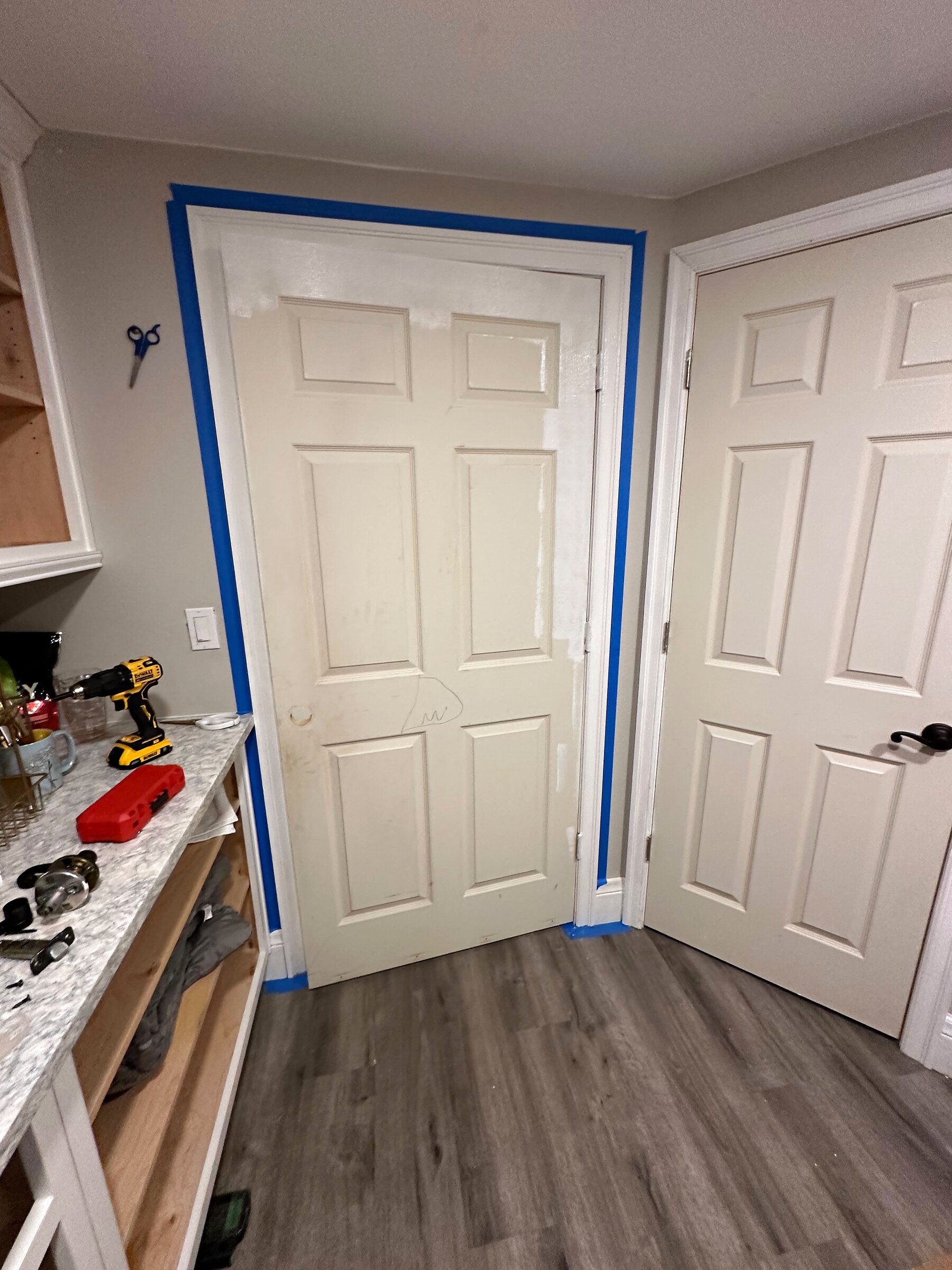 Interior six-panel door and frame masked with blue painter's tape, prepped for painting
