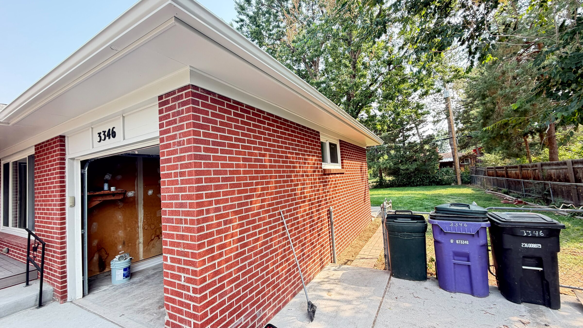Side exterior of the finished brick ranch home with garage and mature trees