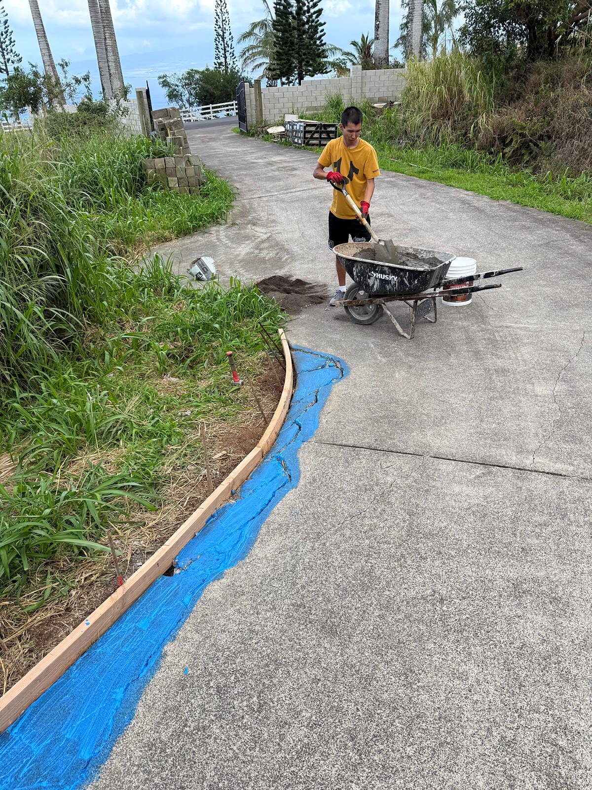 Worker mixes and pours concrete from a wheelbarrow into the curb form along the finished road edge