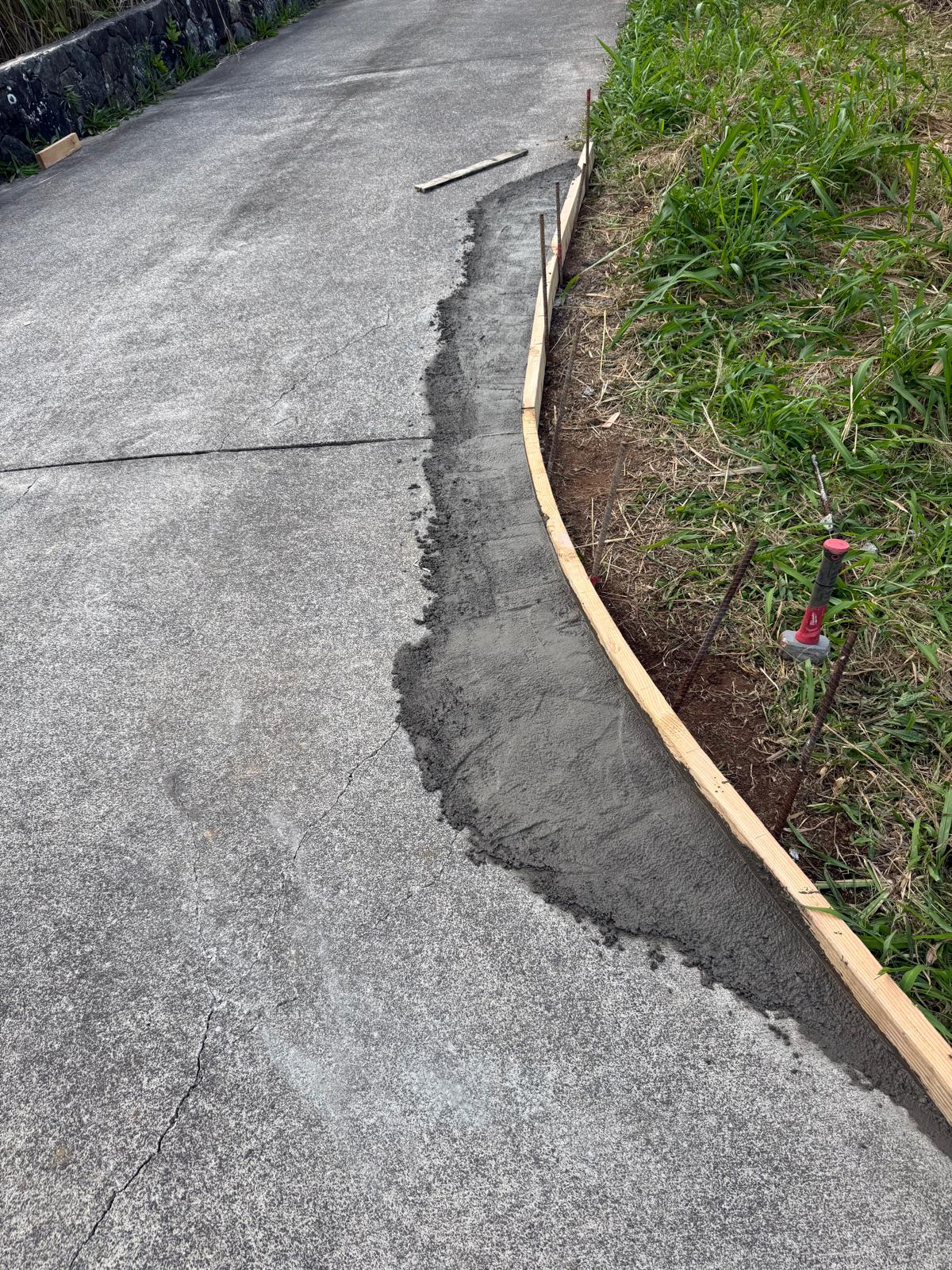 Freshly poured concrete curb troweled smooth against wooden forms and rebar stakes along a driveway edge