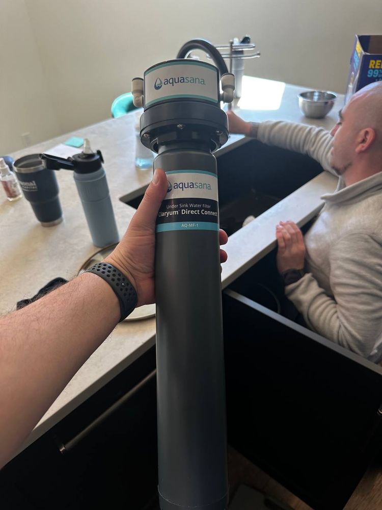Aquasana Claryum under-sink water filter unit held up before installation in a kitchen