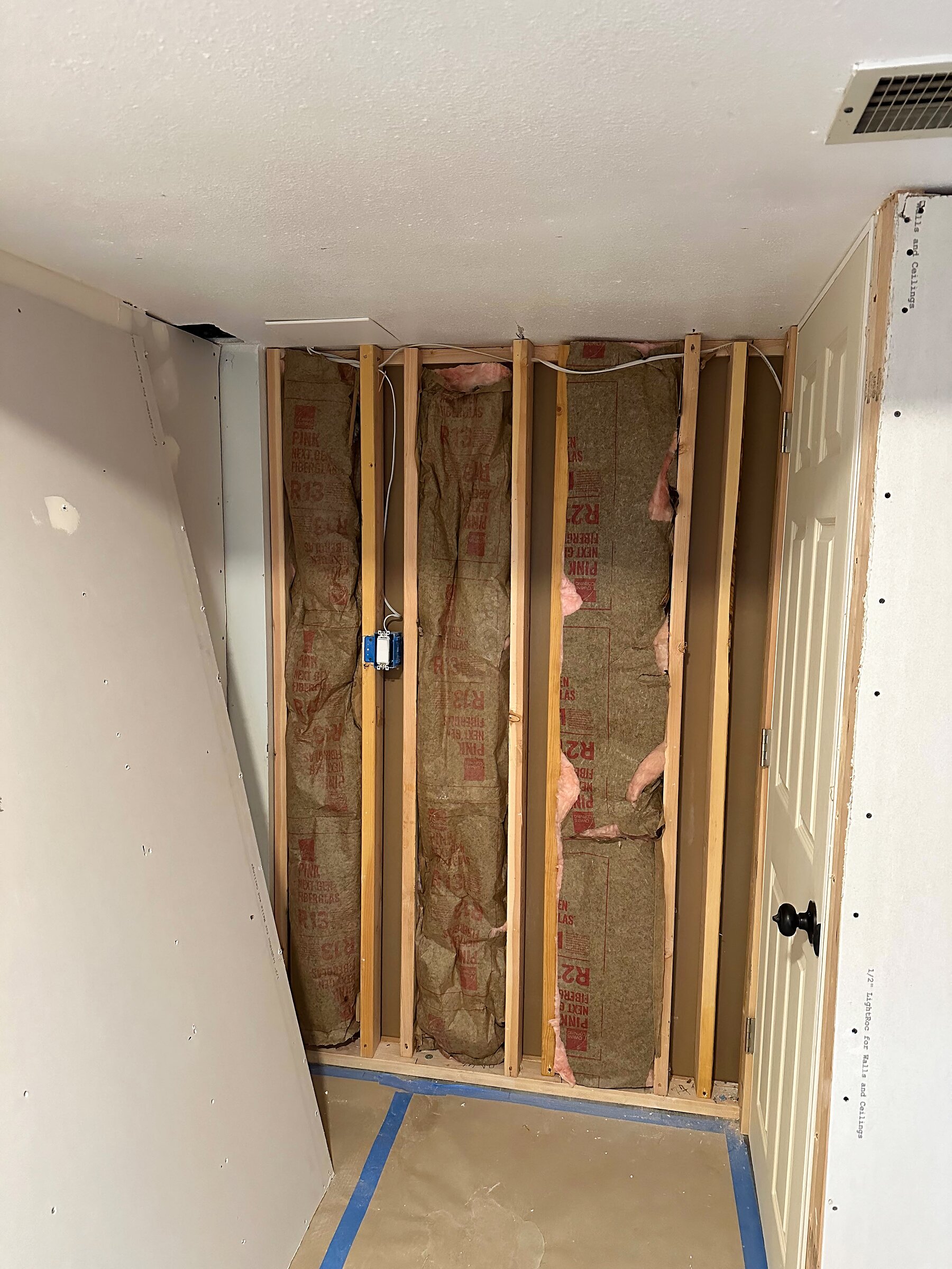 Basement wall opened to studs with new pink fiberglass insulation and wiring run before drywall goes back up