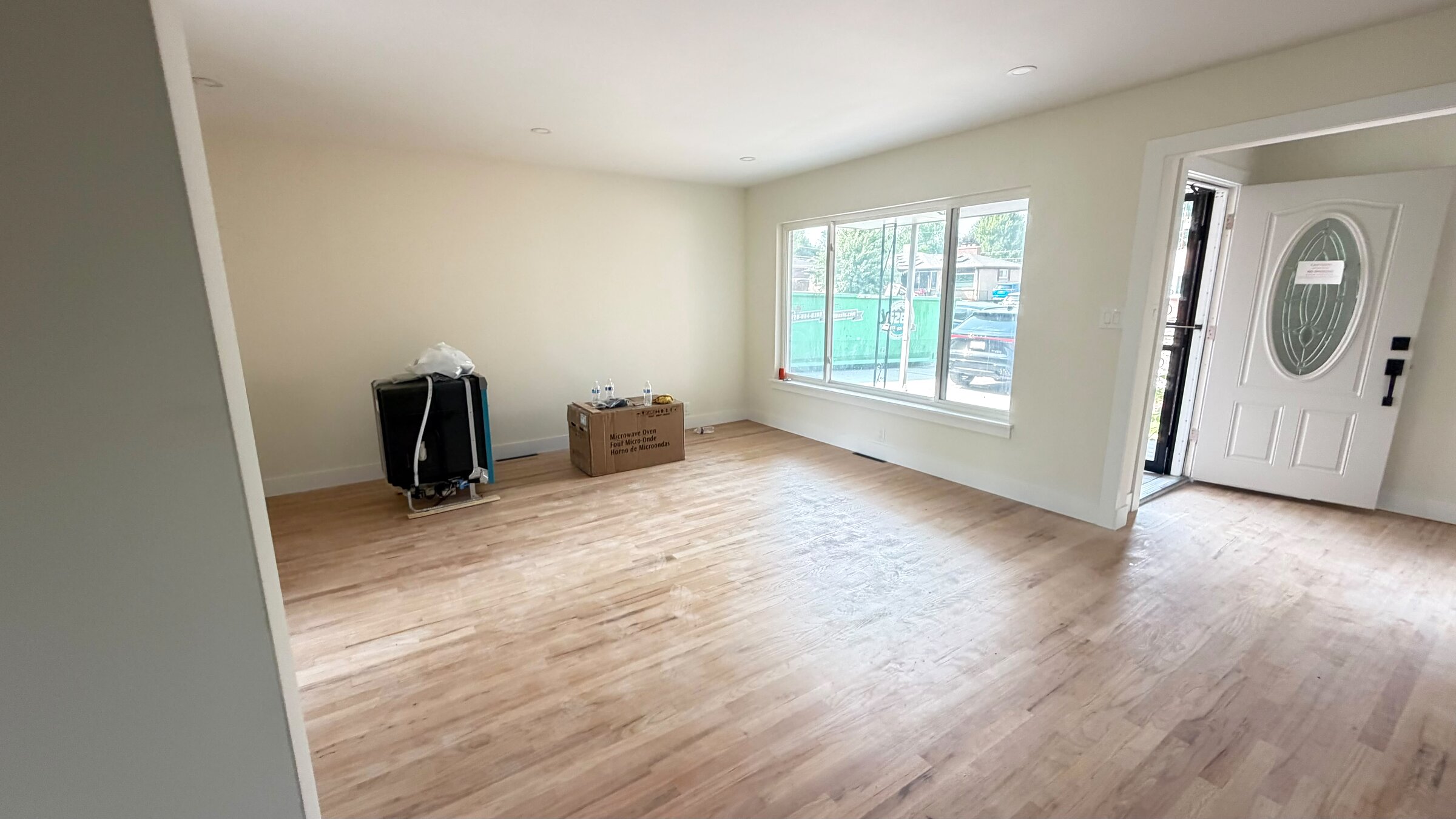 Living room with refinished floors, front entry door, and new appliances staged for install