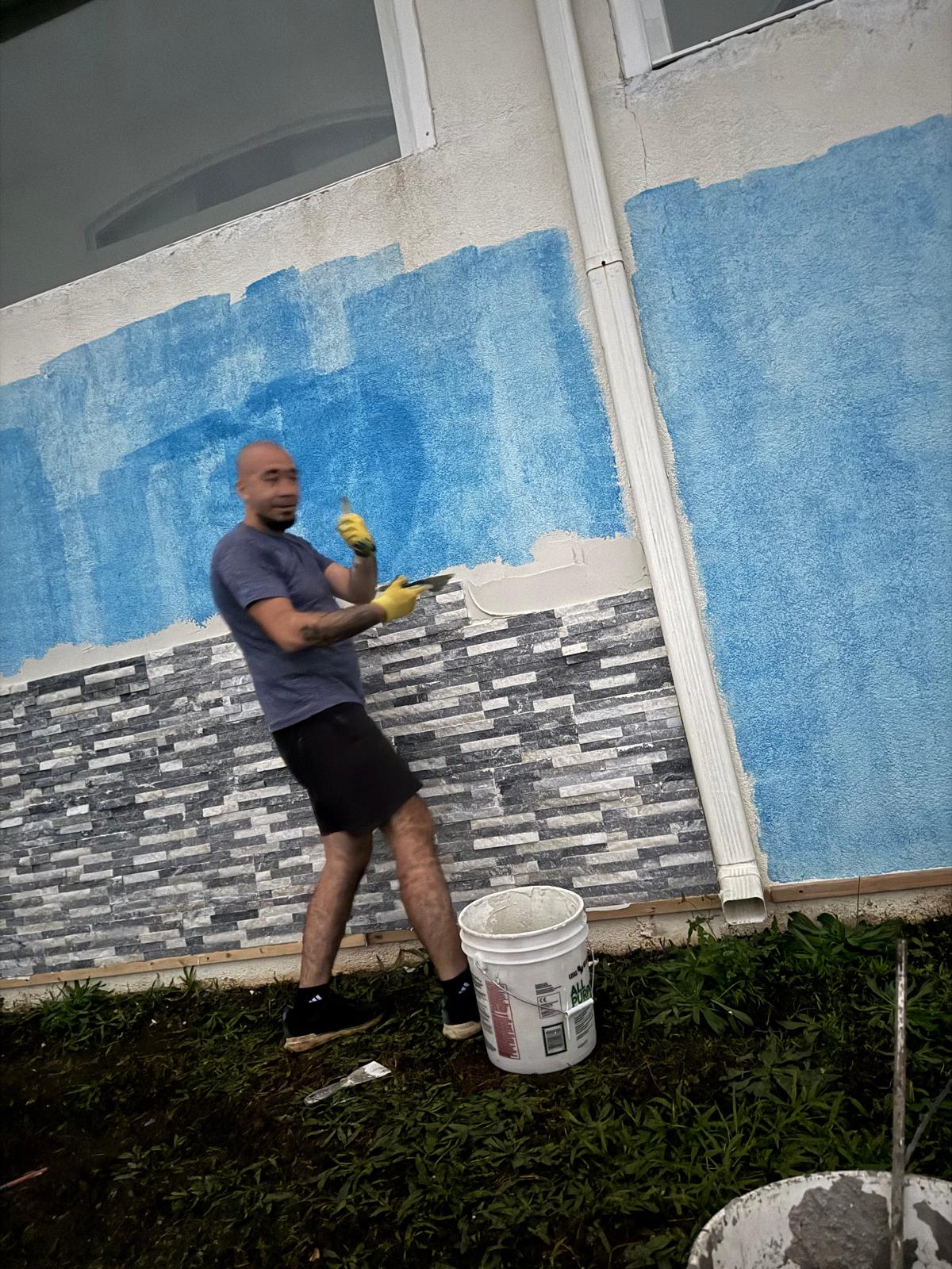 Painter rolling a blue accent coat on an exterior stucco wall above new stone veneer