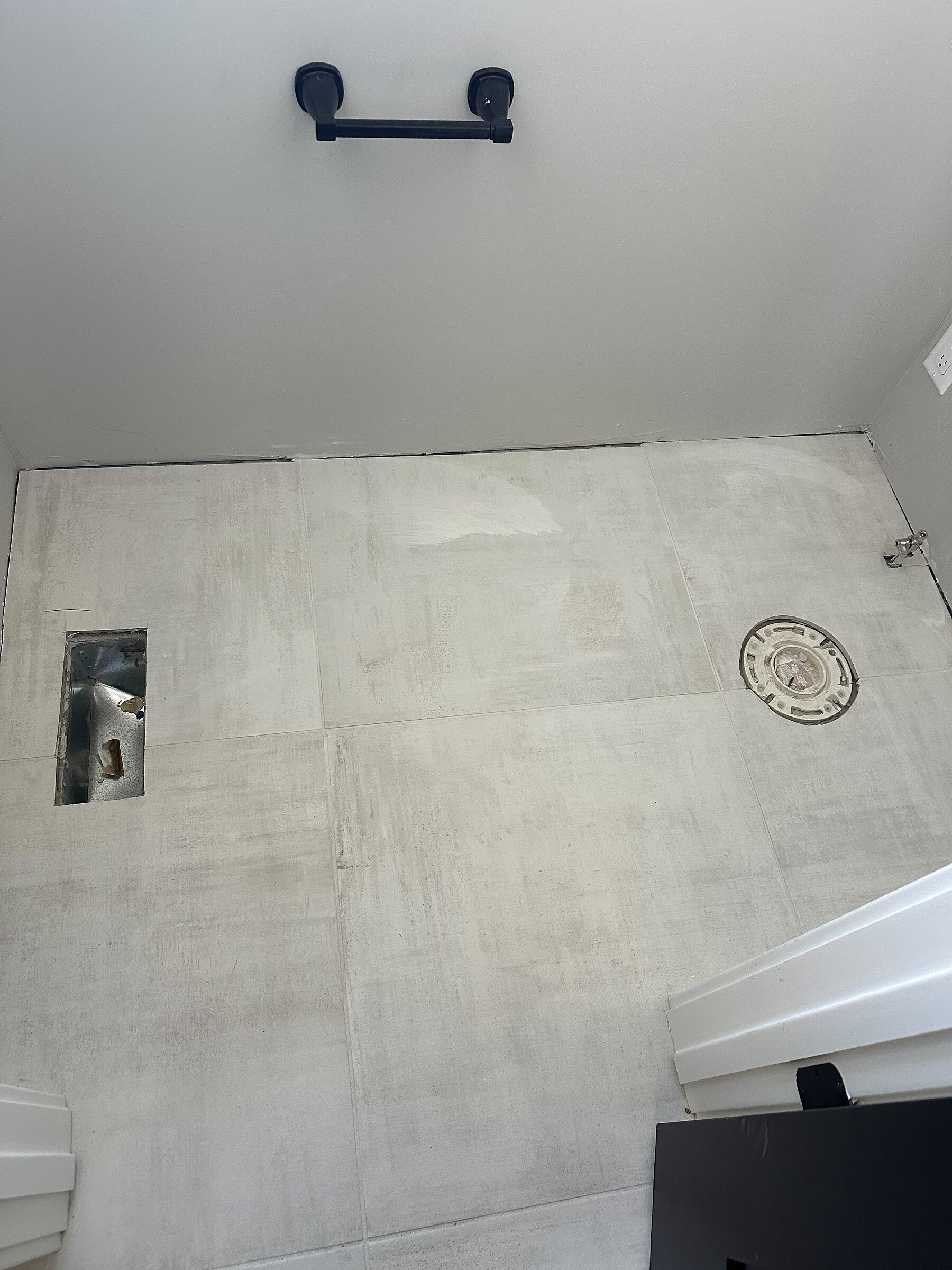 New large-format tile bathroom floor with toilet flange and drain access prepped for fixture install
