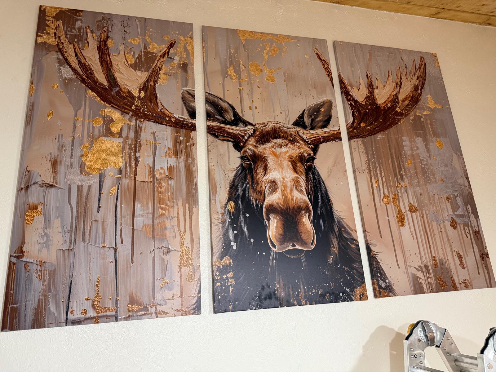 Finished three-panel moose canvas triptych hung evenly spaced and level on a stairwell wall
