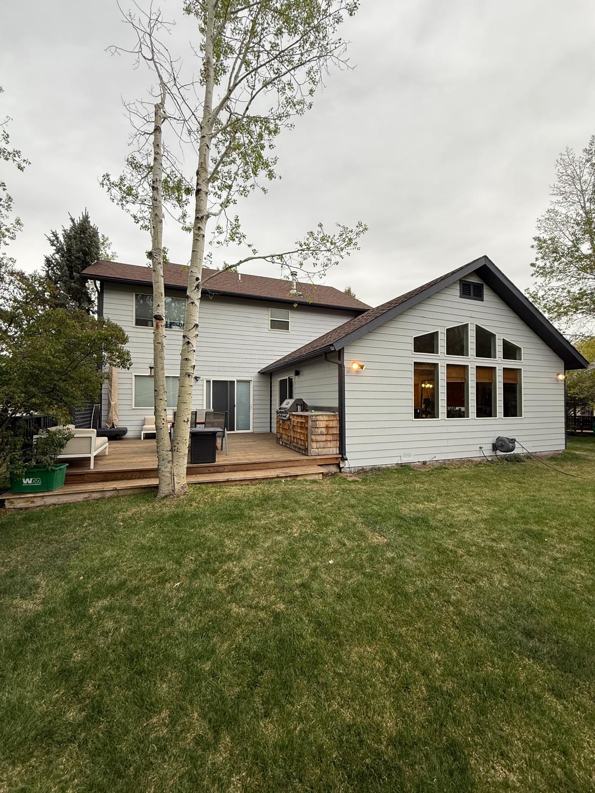 Rear elevation of a two-story home after a full exterior repaint in light gray with dark trim and a cedar deck