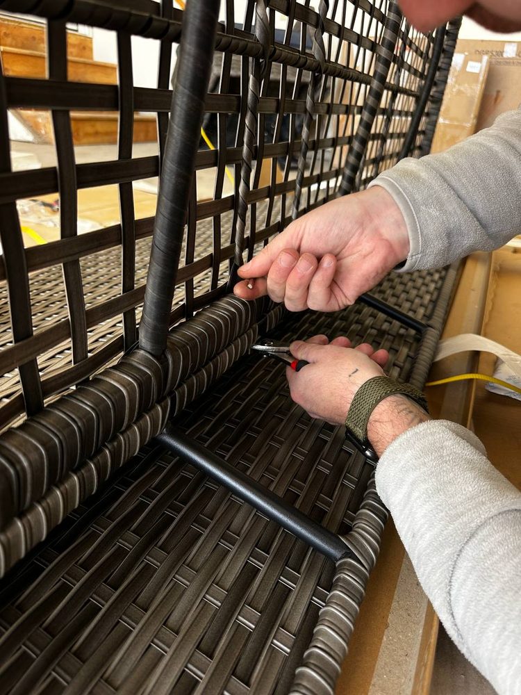 Close-up of pliers securing the metal frame under a wicker patio chair during assembly