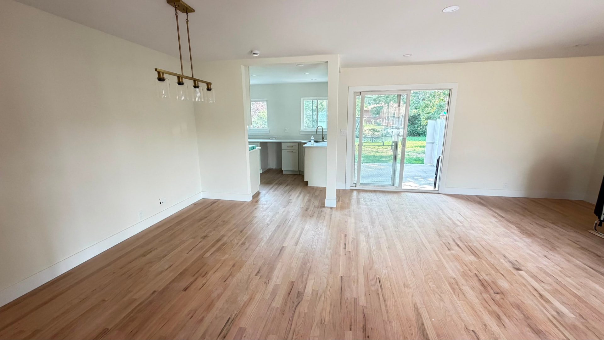 Completed Denver living and dining area with new hardwood flooring, finished kitchen beyond and a sliding glass door