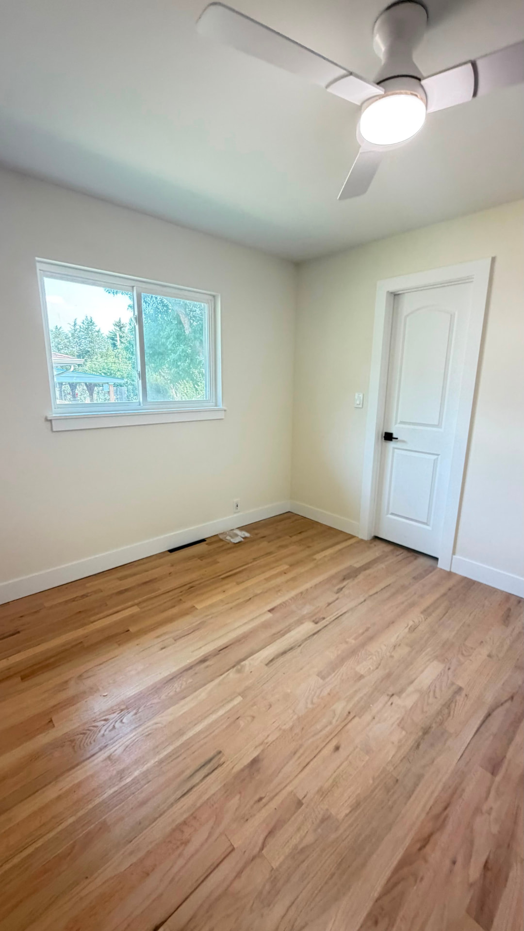 Completed bedroom with white ceiling fan, window, paneled interior door and new hardwood flooring