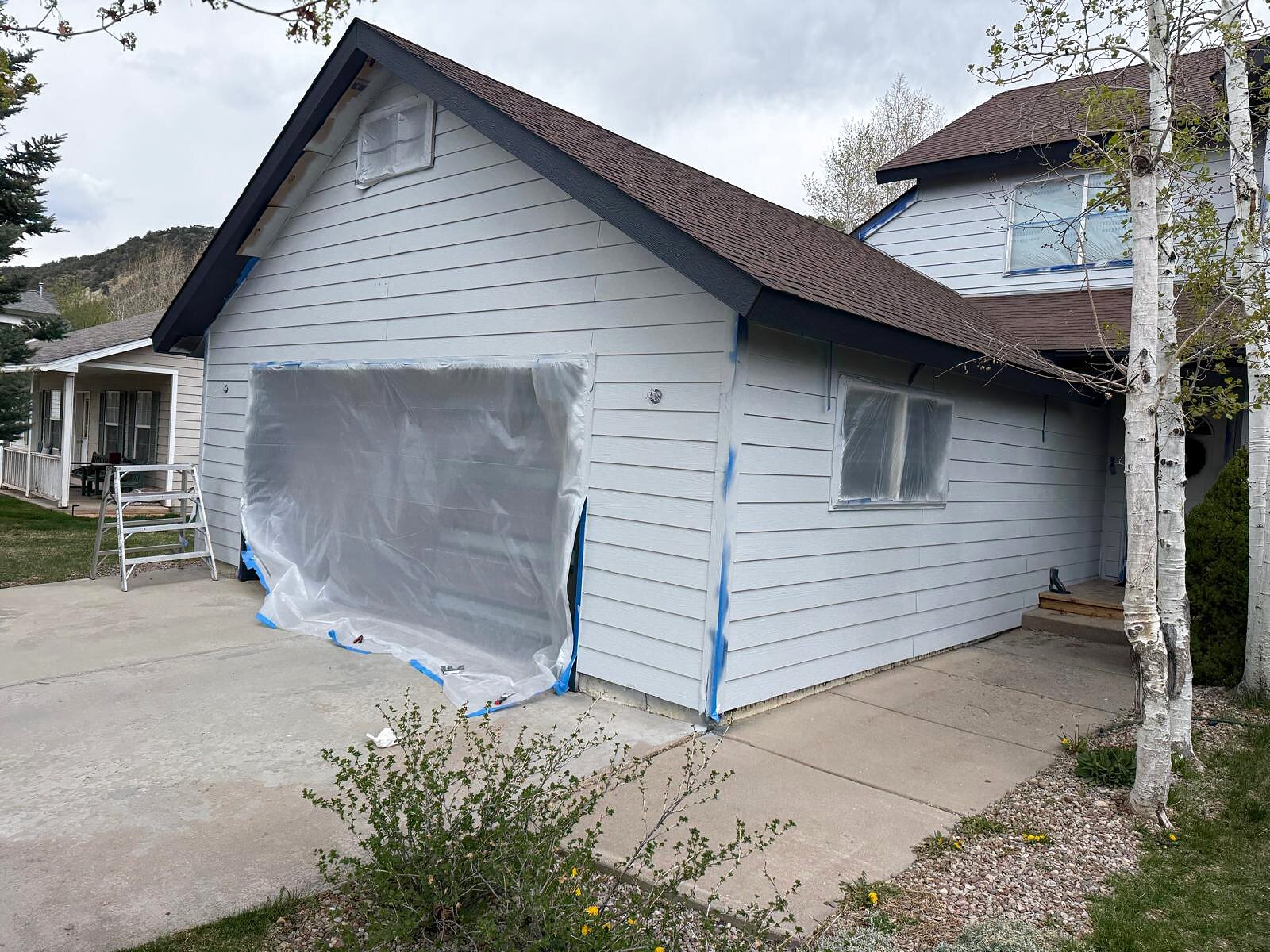 Garage and upper-story exterior with windows fully masked ahead of a fresh coat of paint