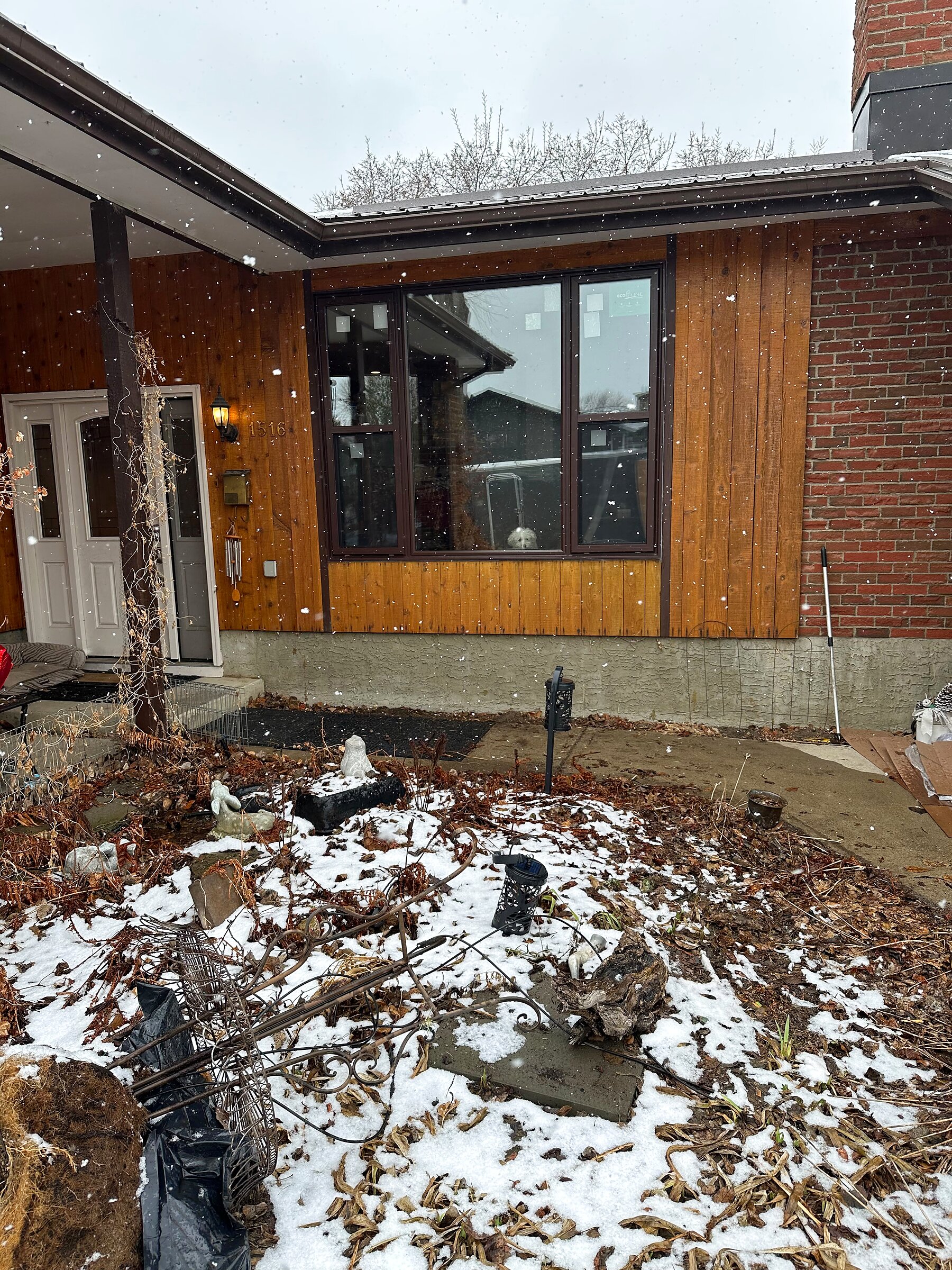 Wood-sided home with a newly installed dark-framed picture window, photographed during light snowfall