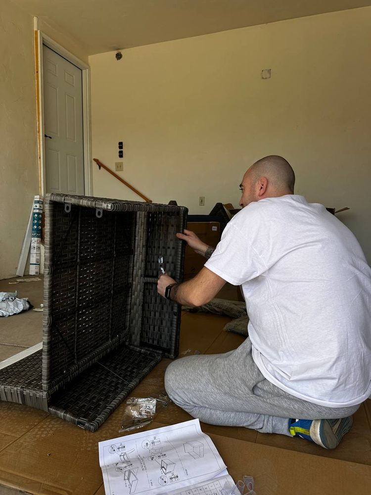 Technician assembling a wicker patio storage box on the floor with instructions laid out