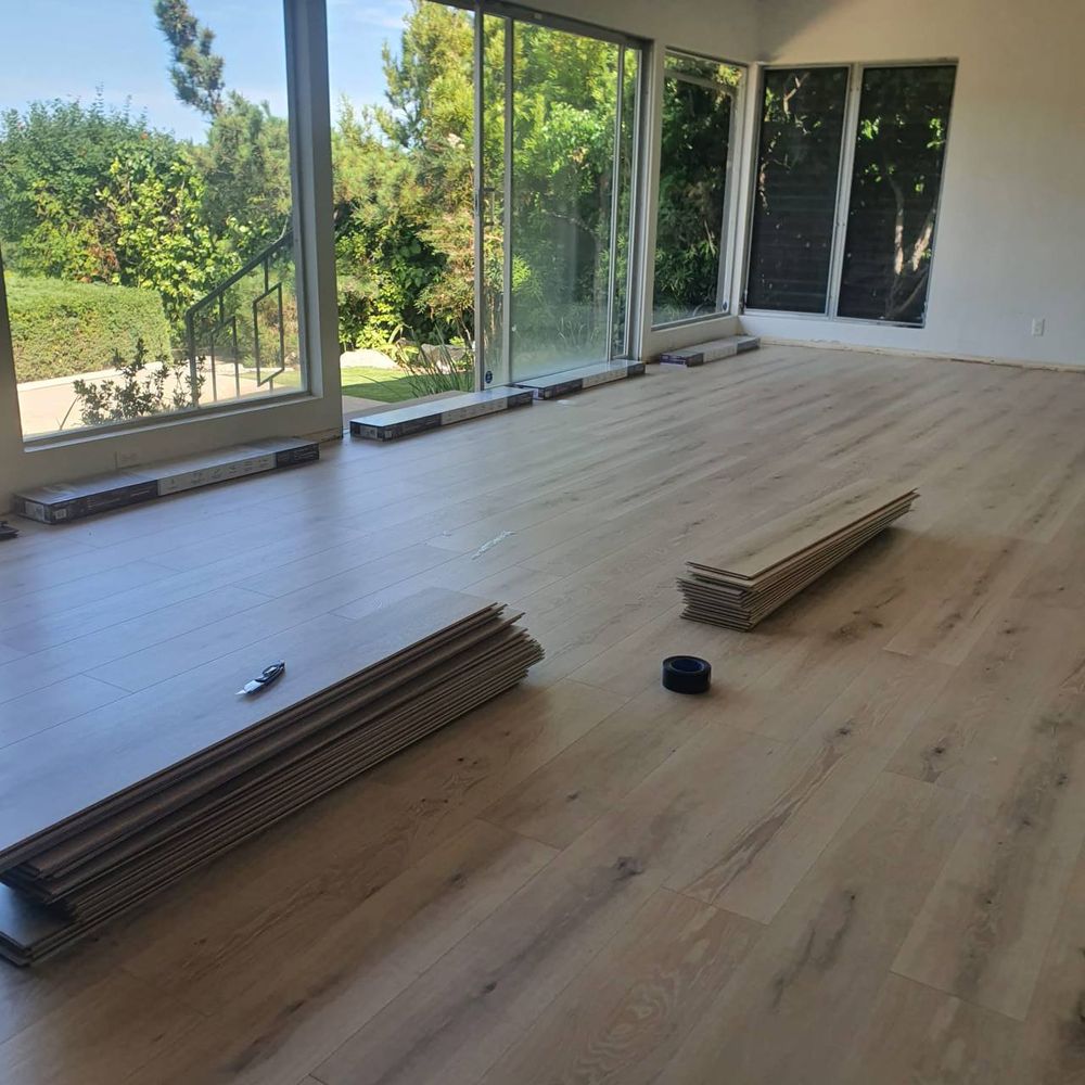 Completed wide-plank laminate floor in a sunlit living room with sliding glass doors and leftover plank bundles