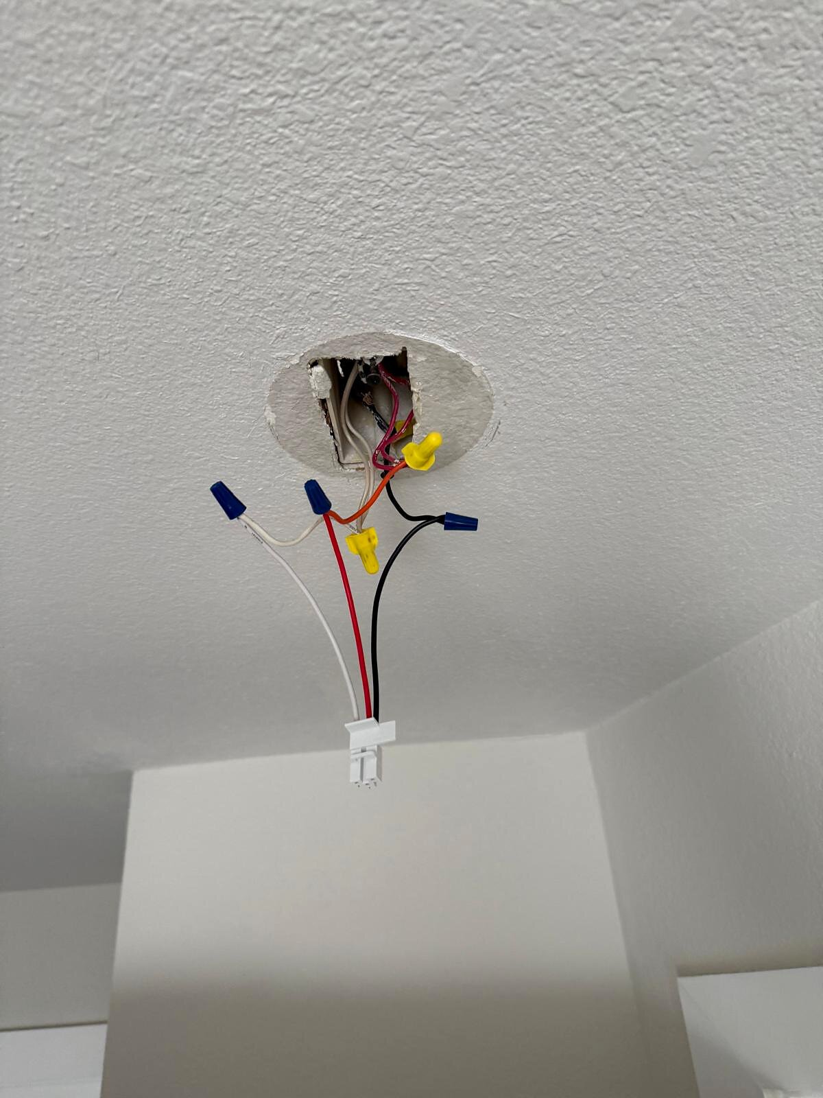 Ceiling junction box with wires capped in nuts and connector, hanging ready before a light fixture is mounted
