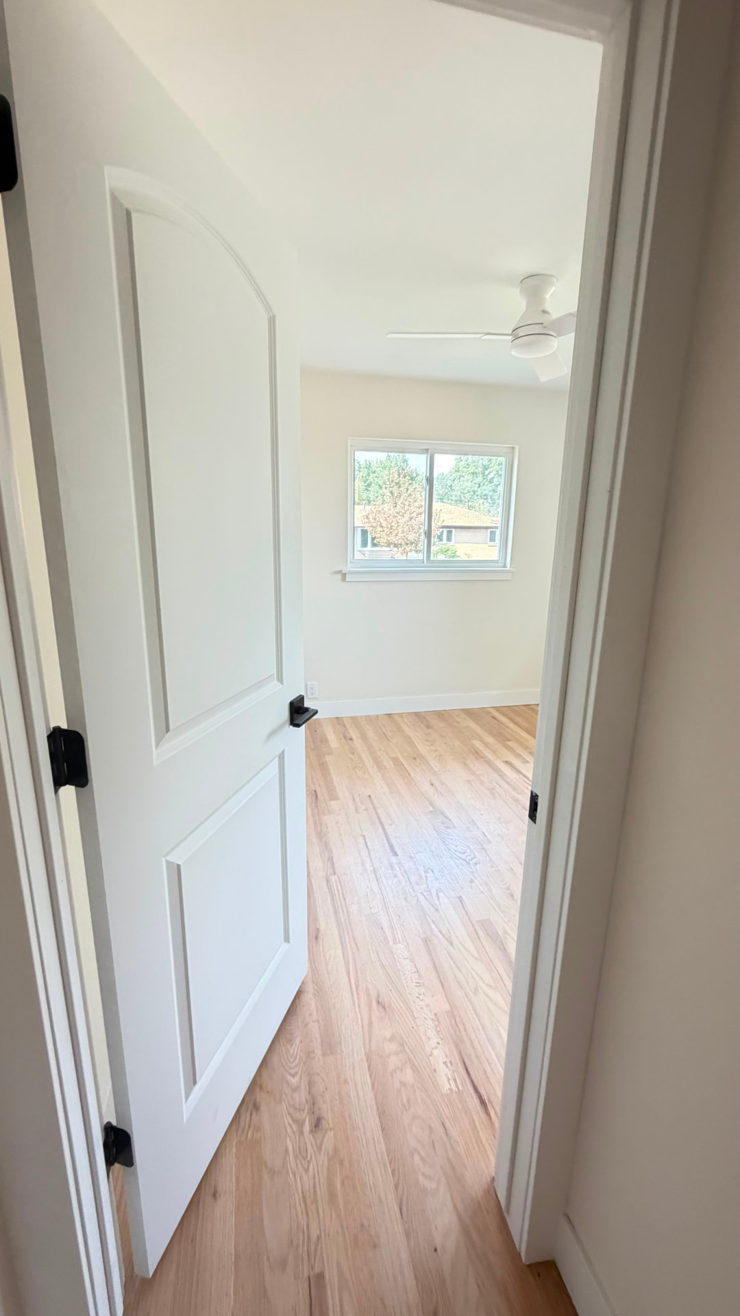 Finished bedroom doorway with white paneled door, black hardware, white trim and new hardwood flooring