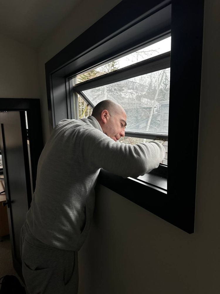 Technician checking the operation of a black-framed casement window from inside a room