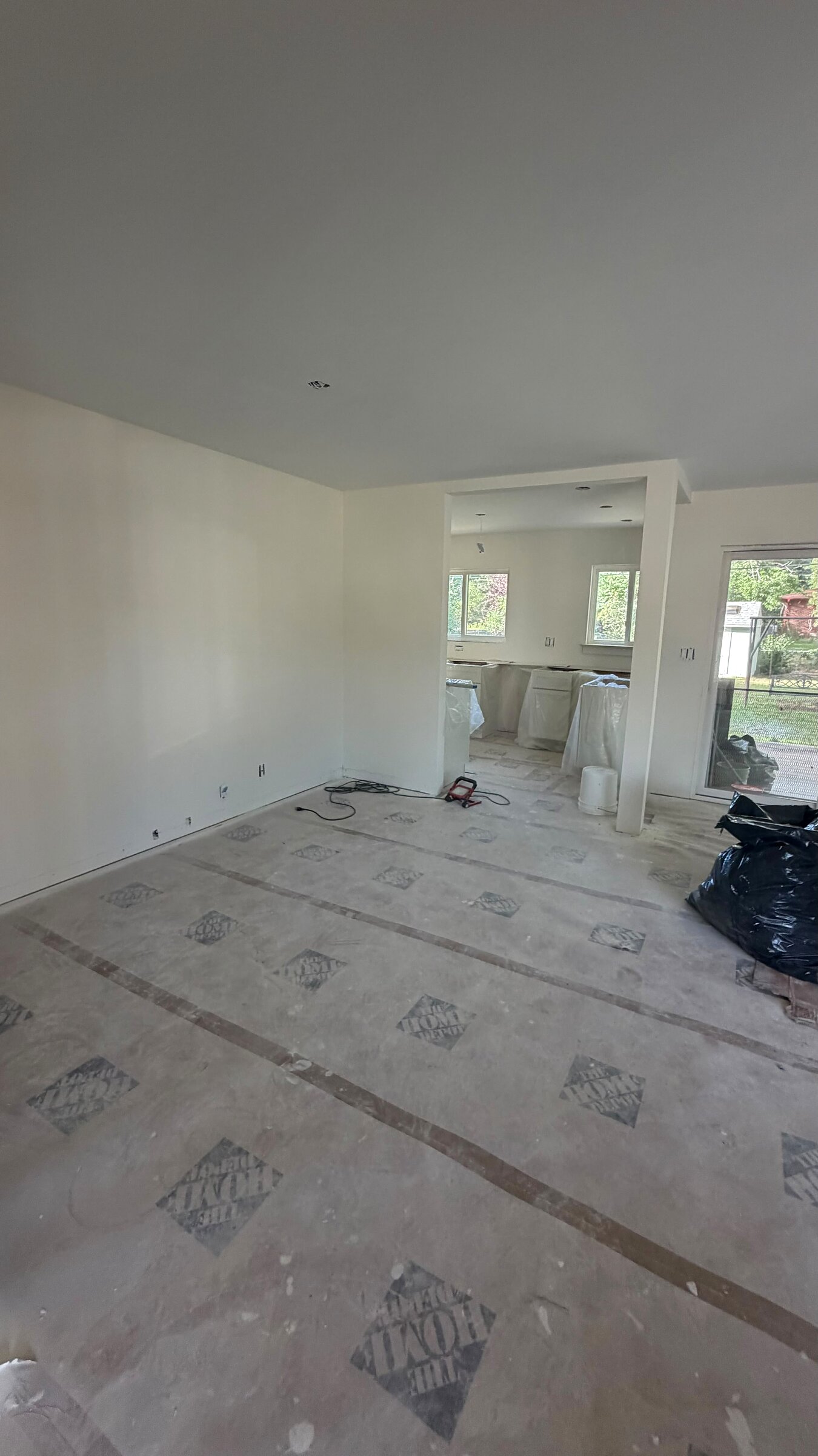 Living room subfloor prep with a view through to the kitchen, cabinets wrapped for protection
