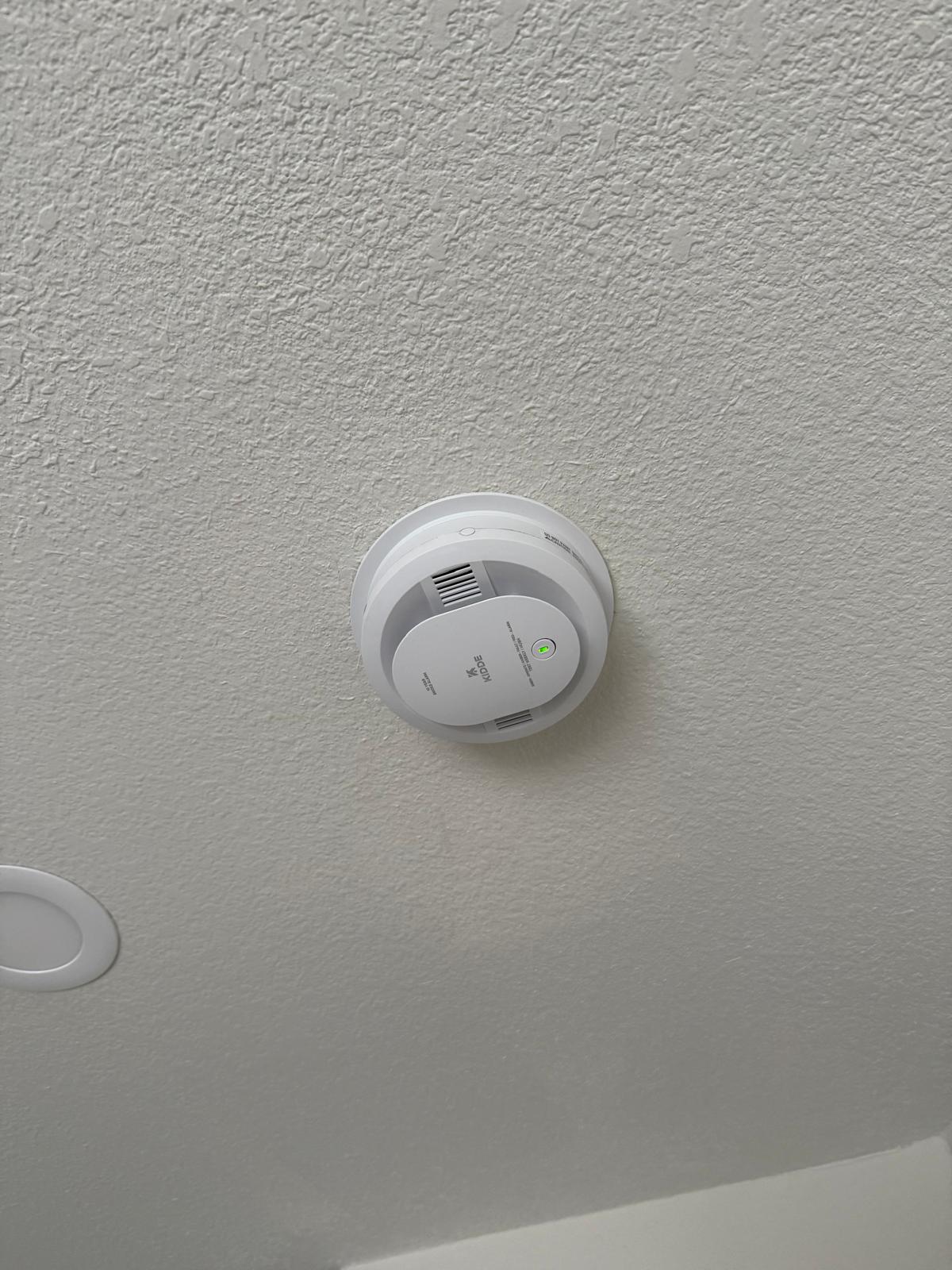 New Kidde smoke detector mounted and powered on a freshly textured ceiling