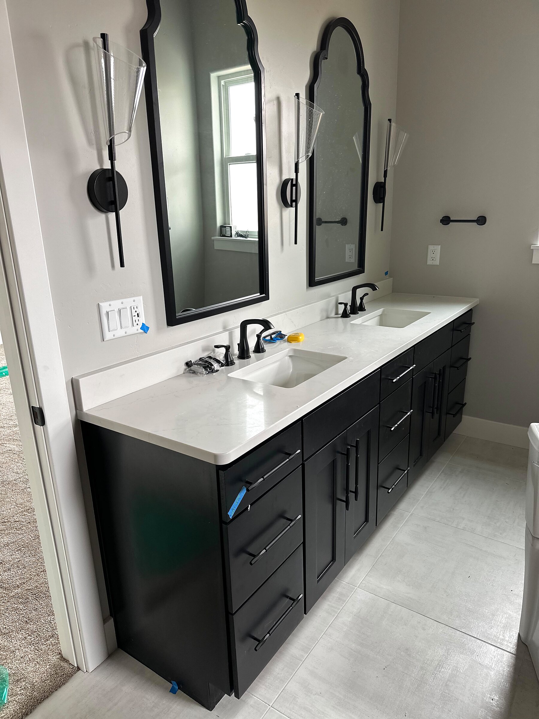 Double vanity with black cabinetry, quartz counters, black fixtures and arched mirrors with sconce lighting
