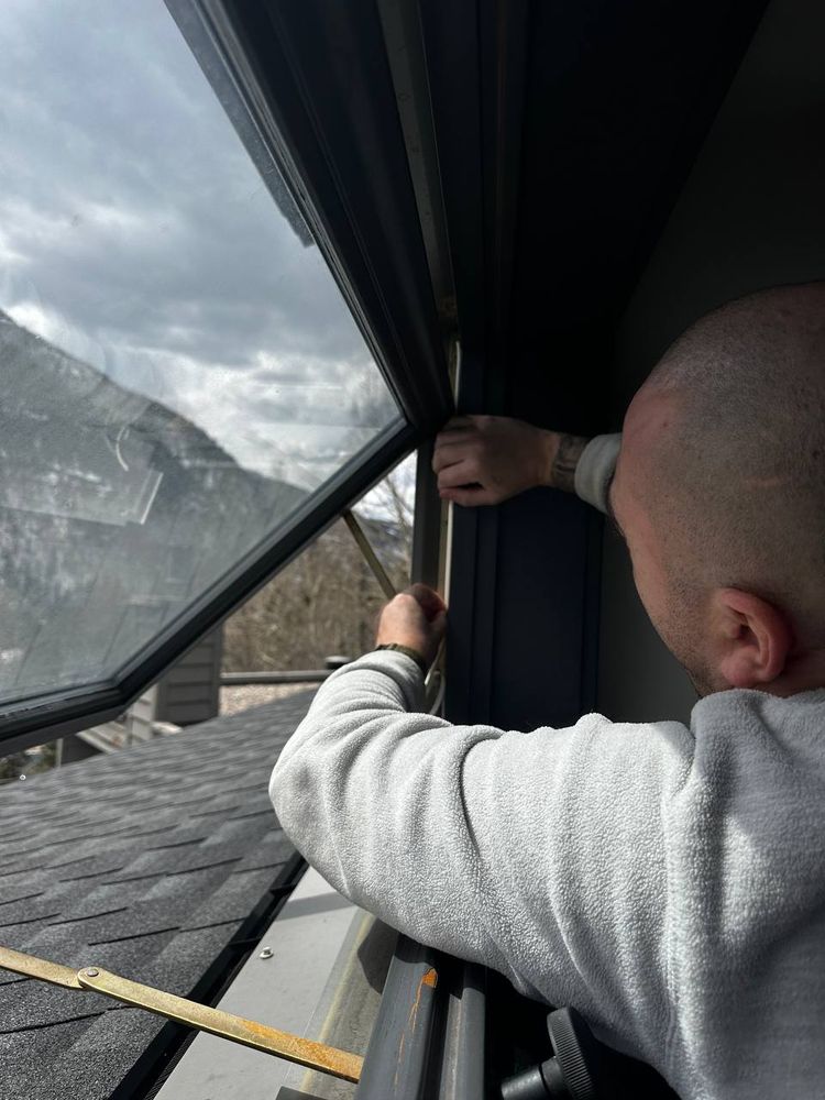 Technician resealing the frame of a large picture window overlooking a mountain roofline