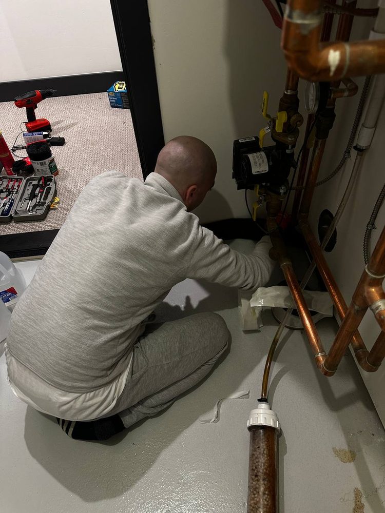 Technician kneeling to hook up a whole-home water treatment system under copper manifold piping