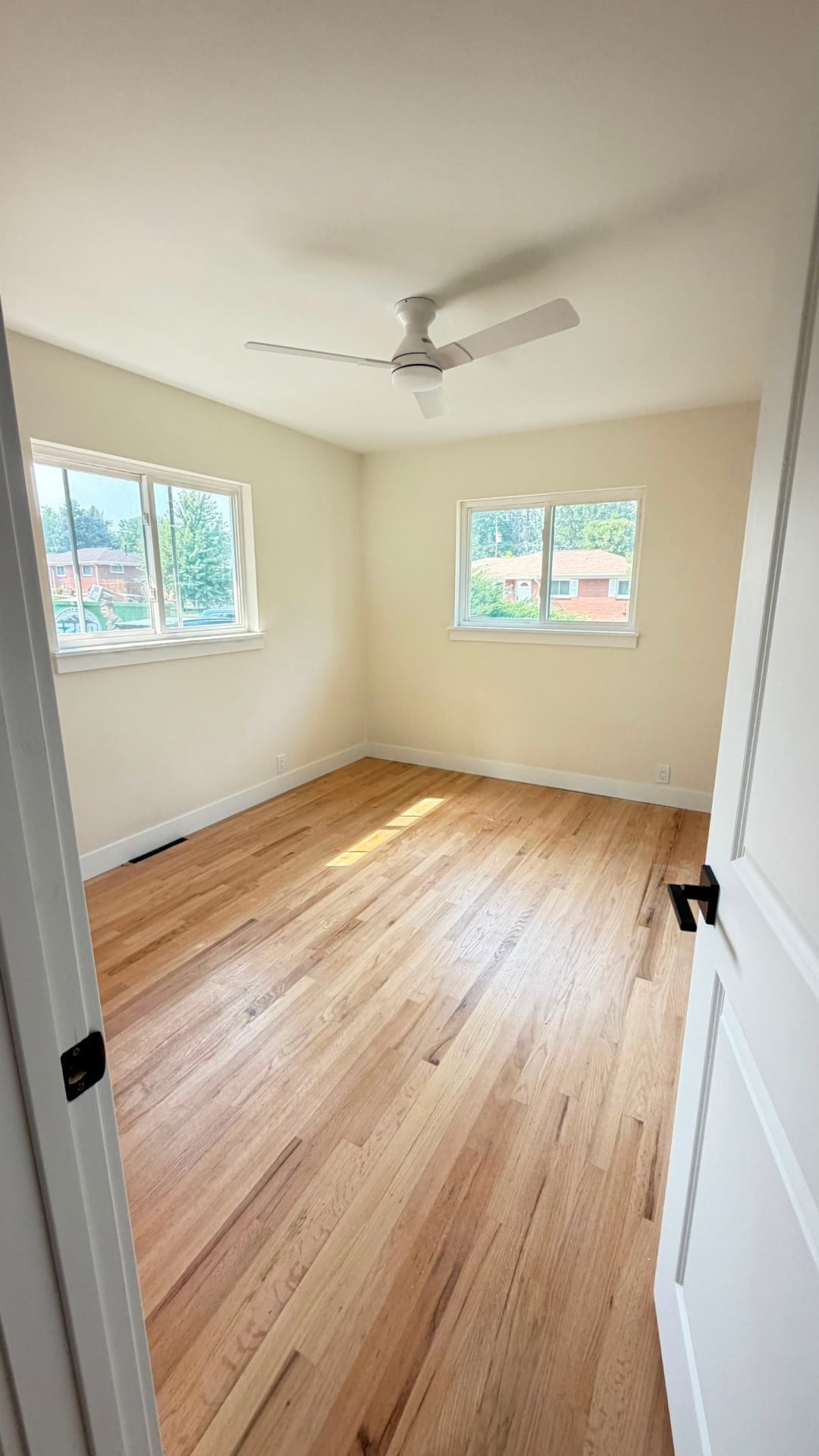 Completed bedroom with two windows, white ceiling fan, finished walls, trim and new hardwood flooring