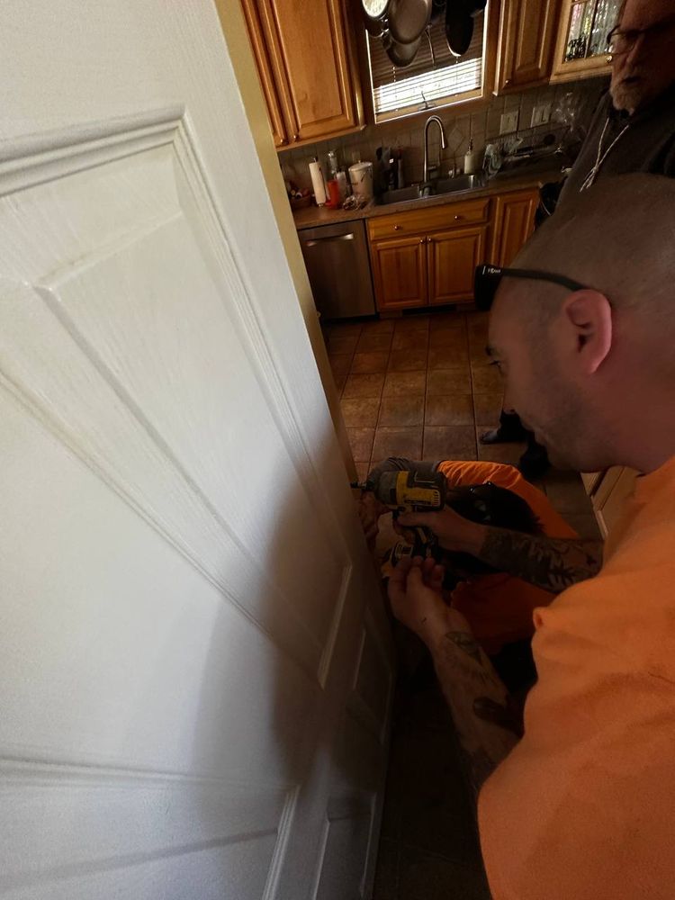 Installing hinge hardware on a white interior door with a drill in a kitchen doorway