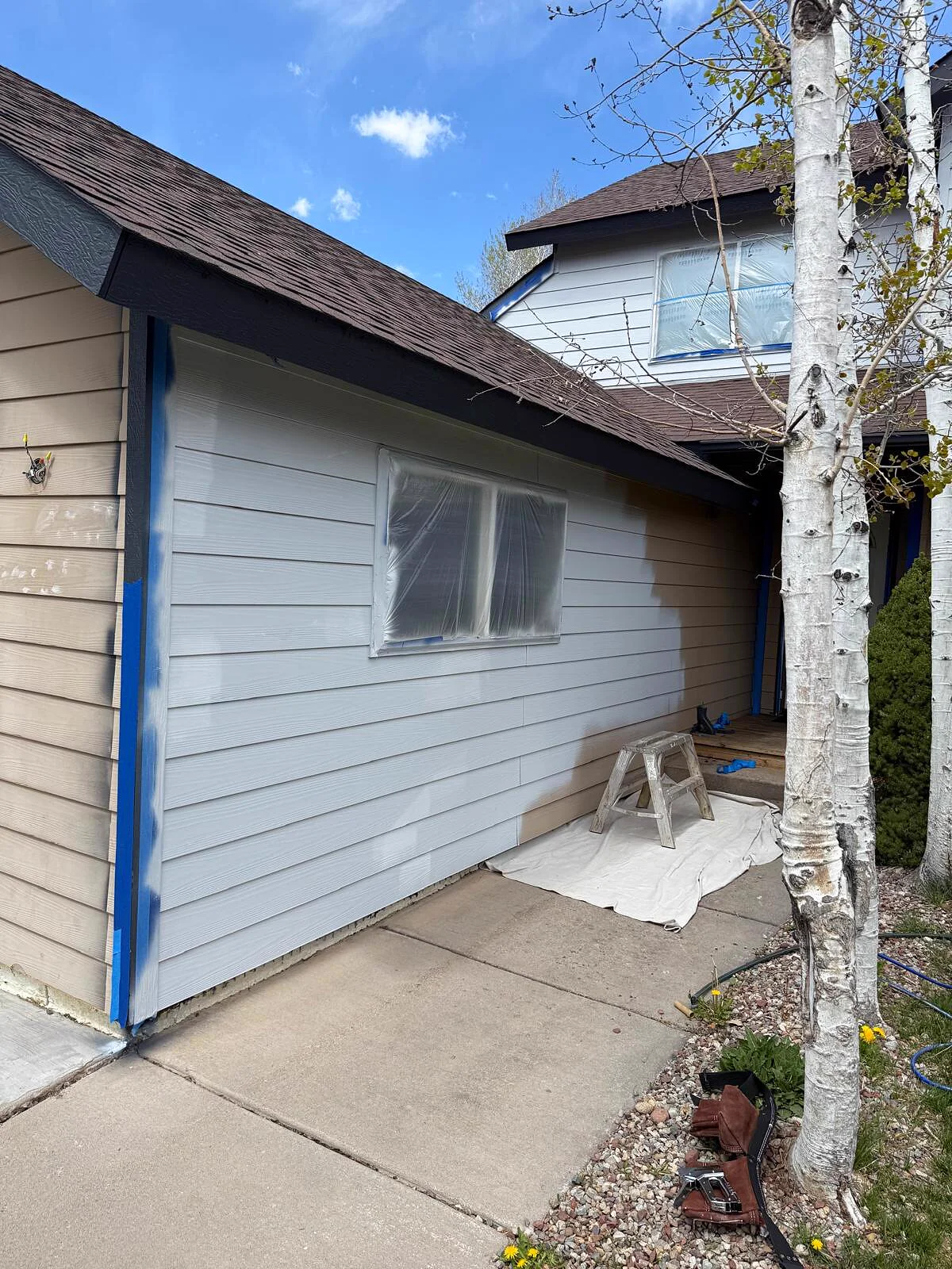 Home exterior mid-repaint, fresh light gray siding color applied over the original tan