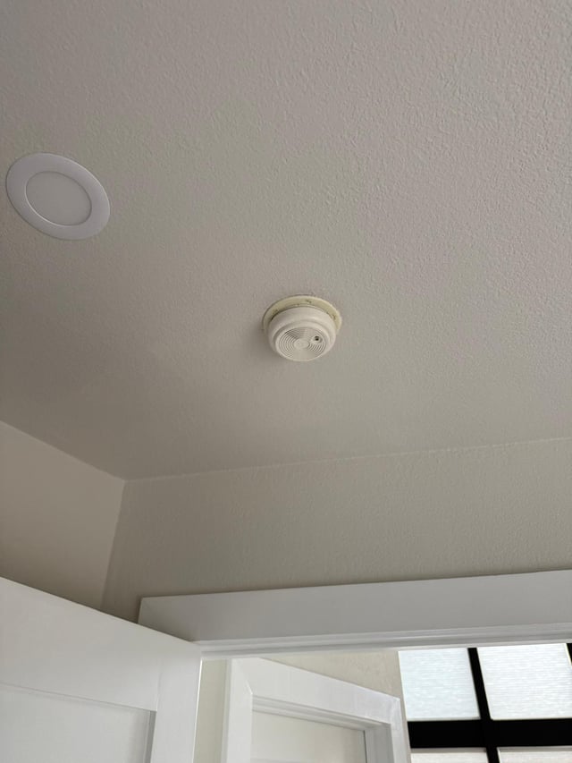 Original yellowed smoke detector on a bedroom ceiling before replacement