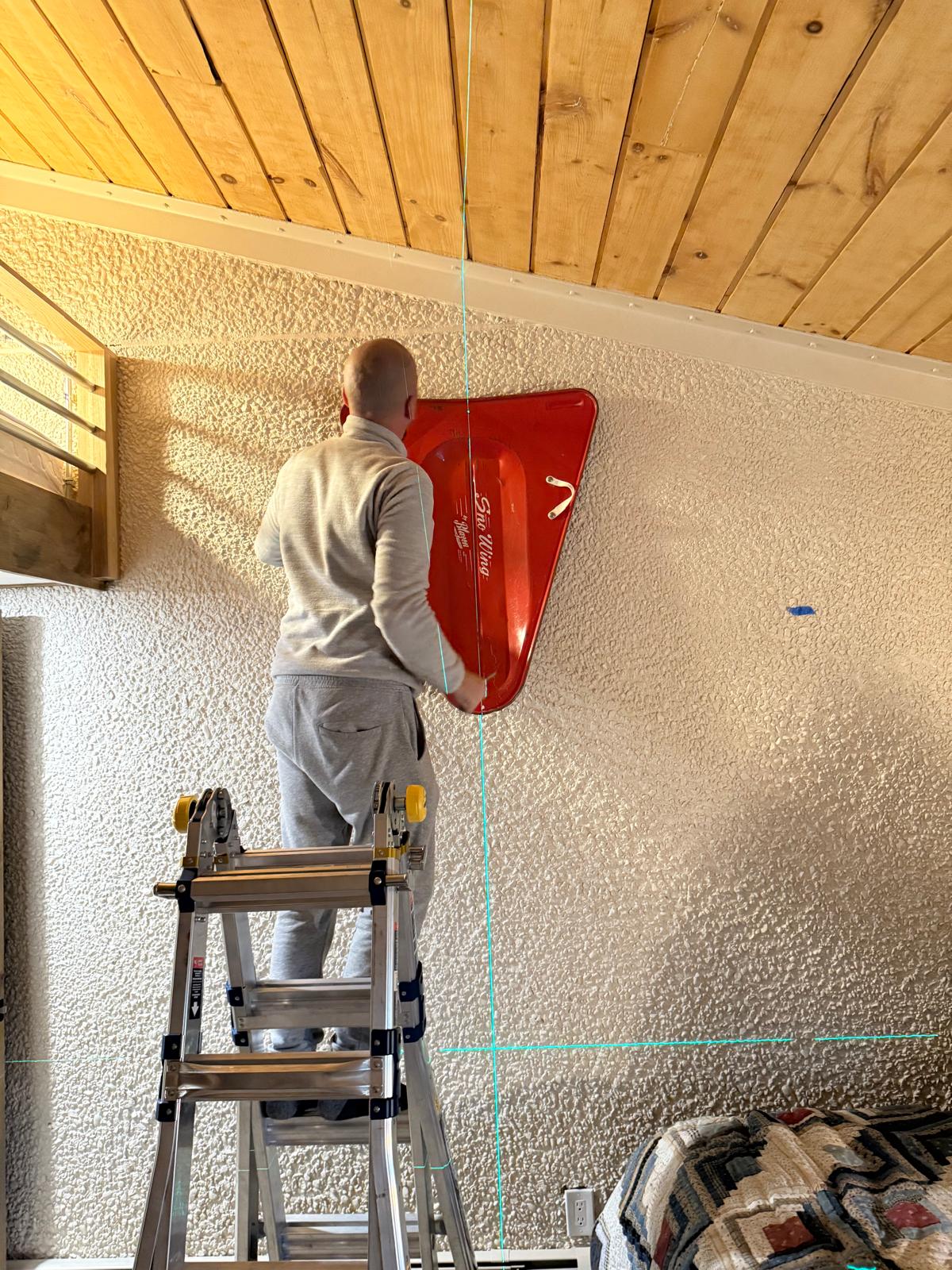 Technician setting a vintage red sled on a textured wall using laser cross-lines for layout
