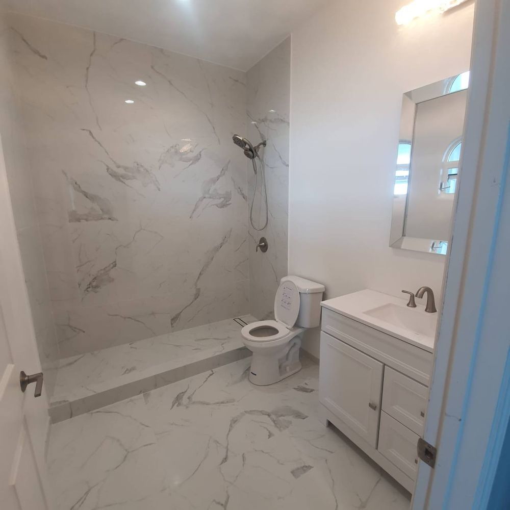 Finished bathroom with large-format marble-look tile shower, white vanity and framed mirror