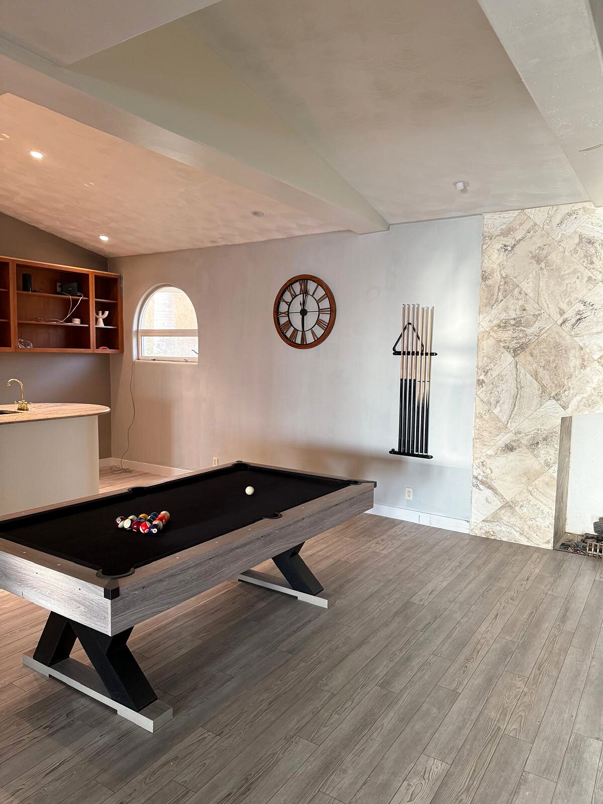 Finished pool room with stone accent wall, wall-mounted cue rack, wood flooring, and pool table racked and ready