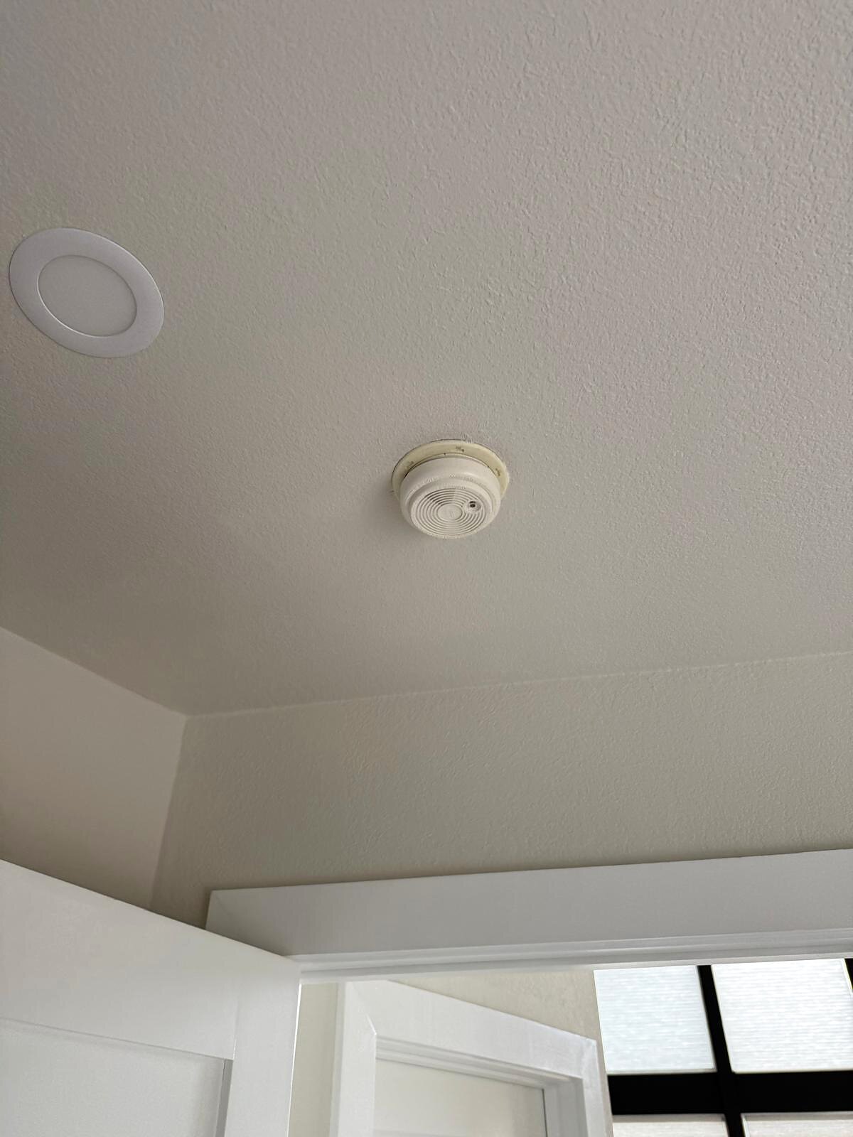 Close-up of a new smoke detector mounted on the ceiling near a recessed light fixture