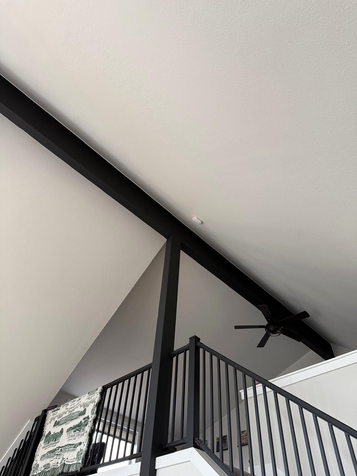 Vaulted ceiling with a black beam, recessed can light, and a newly installed smoke detector overhead